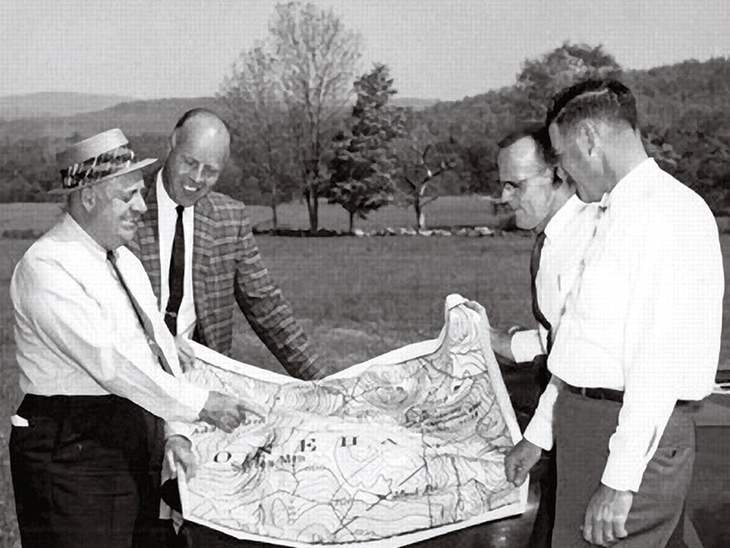 Four men look over a map while in a field