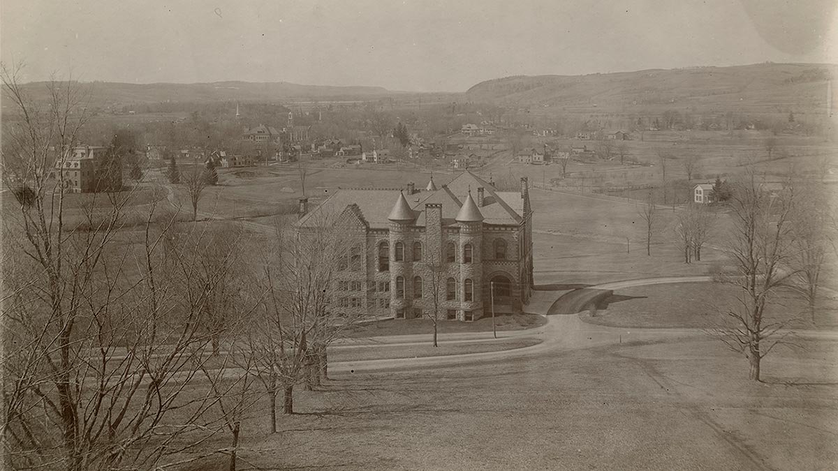 Black and white photo of James B. Colgate Hall and the valley below, seen from partway up the hill