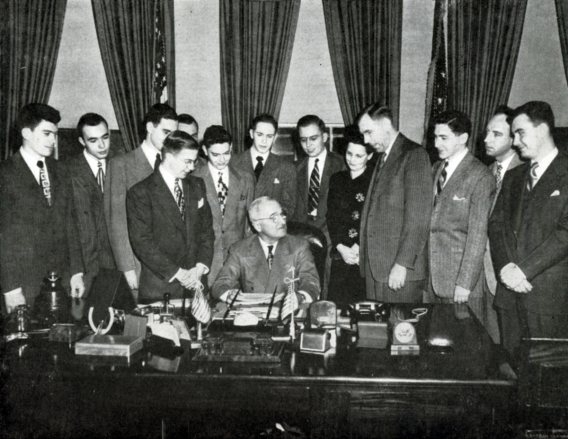 A class of students stands behind Harry Truman in the Oval Office