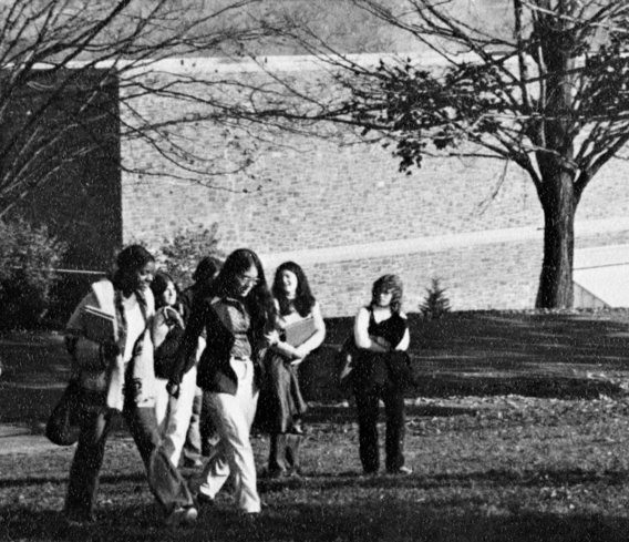 Female students walk across campus in front of a stone academic building