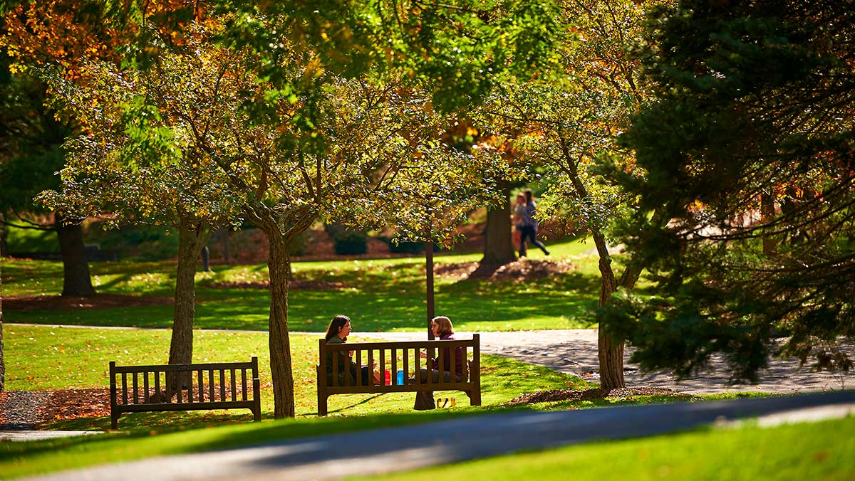 Students converse on a bench on the quad amidst fall foliage