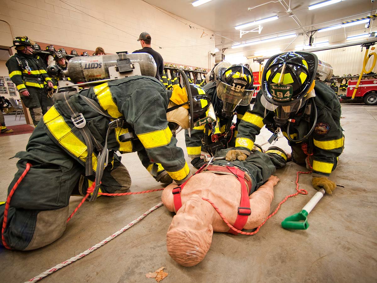 Firefighters in full gear practice life-saving techniques with a dummy